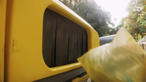 Hand Throws Trash into Yellow Recycle Bin