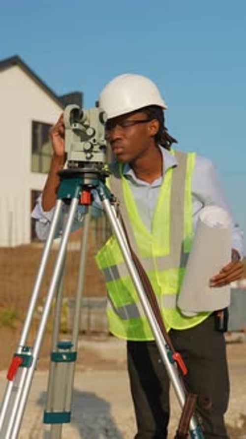 Professional Surveyor Using Theodolite on Construction Site Near New Cottage