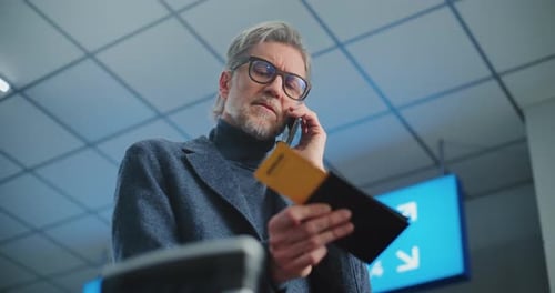 Crowded International Airport Terminal Mature Man Holding Plane Ticket Talking By Mobile Phone
