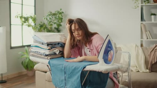 Tired Woman Resting Head on Hand at Ironing Board