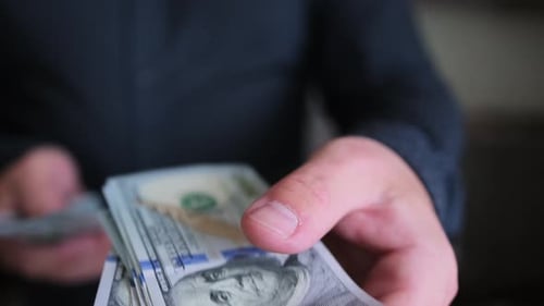 Man's hand holds out stack of American one hundred dollar bills to another person, close-up