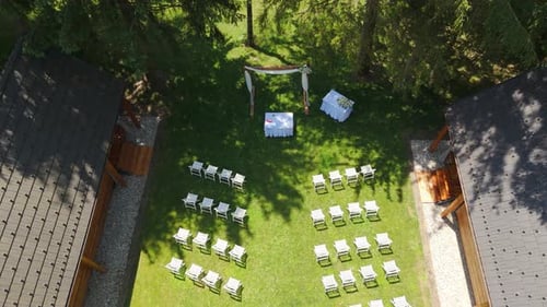 Aerial: wedding ceremony with an arch and white chairs during the day in the forest