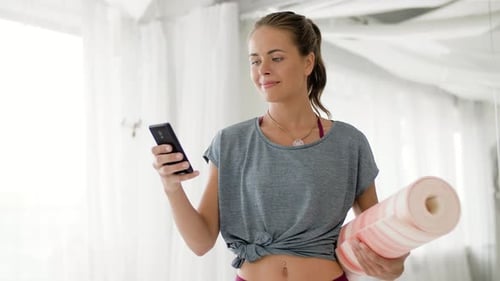 Smiling Woman with Yoga Mat Using Smartphone