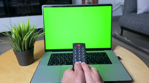 Turning On the Future — Remote Control Activating Green Screen Laptop in Cozy Setup.