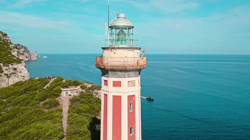 Nahaufnahme eines Leuchtturms, der über dem Meer thront, mit felsigem Ufer und grünem Pinienwald im Hintergrund