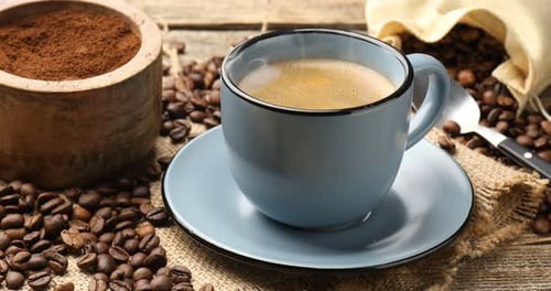 Aromatic coffee in cup and beans on wooden table, closeup