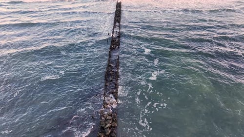 Breakwater Extending Into the Ocean Surrounded By Waves and Coastal Scenery By the Shore During