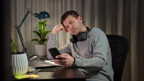 Freelancer Procrastinating at Home Office Scrolling Phone Instead of Working