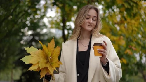 Woman in Cream Coat Holding Autumn Leaves and Coffee