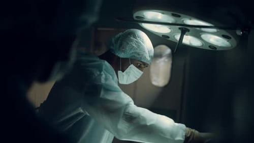 Focused Surgeon Performing Operation in Dark Sterile Hospital Operating Room. Professional Doctor
