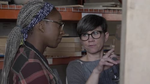 Two Women Discussing Wood in Workshop Environment