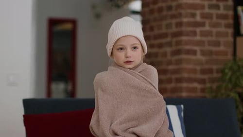 Cozy Child Wrapped in a Blanket and Wearing a Hat in a Warm Indoor Setting During Winter
