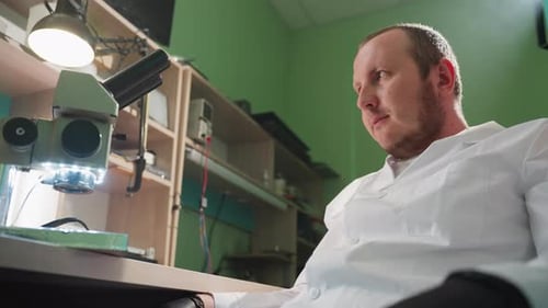 Man Looks At Microscope in Lab Environment