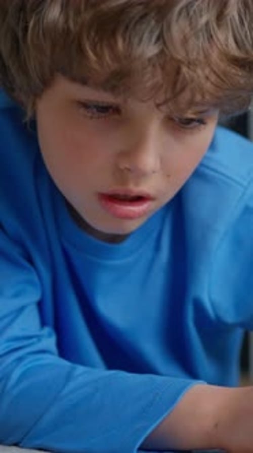Closeup of a Focused Young Boy in a Blue Shirt Concentrating on Schoolwork Writing or Drawing with a