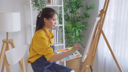 Asian young talented woman artist coloring on painting board in house.