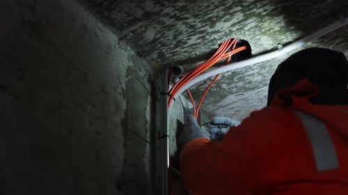 Technician Fixing Wiring In Dark Undercroft