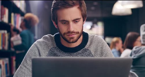Focused Young Adult Studying With Laptop in Library