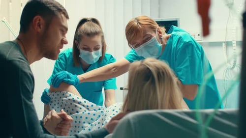 En el hospital, una mujer que da a luz, su esposo la sostiene de la mano en señal de apoyo y los obstetras la ayudan. Modificar