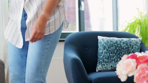 Household, Home Improvement and Cleaning Concept - Woman Arranging Cushions on Armchair