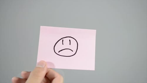 Hand Places Sticky Note with Sad Face Drawing