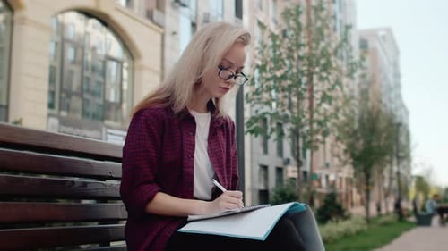 Young Woman Writing in Notebook on Park Bench