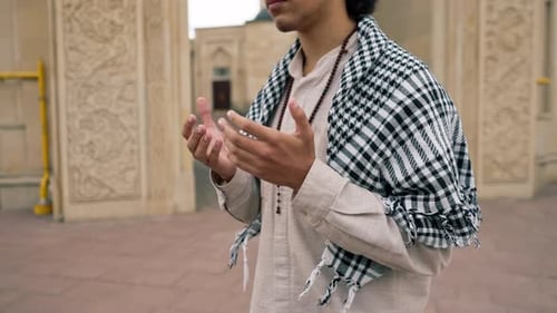 Nahaufnahme eines arabischen Mannes in nationaler Kleidung mit einem Rosenkranz um den Hals, der im Innenhof betet