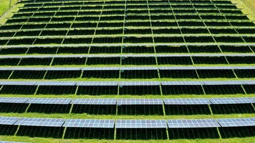 Rows of solar panels on a large green field shot from above on a sunny day
