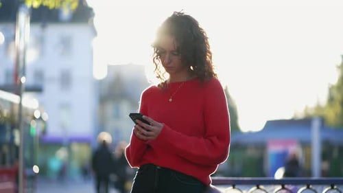 Woman Texting on Phone in City Street leaning on metal rail outdoors. Candid 20s person texting