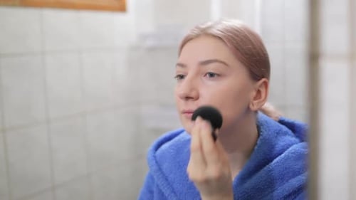 Woman Applying Makeup in Bathroom with Beauty Sponge