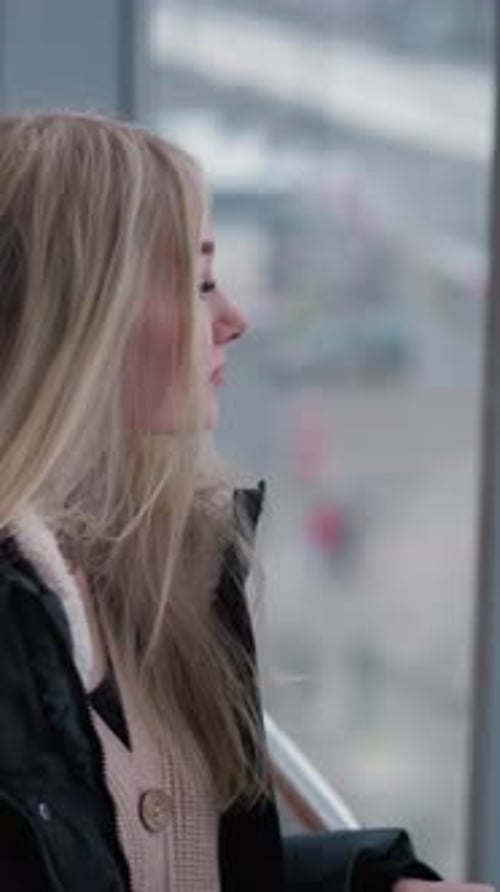 Young Lady Gazing Through Glass Building Window with Urban Cityscape Background