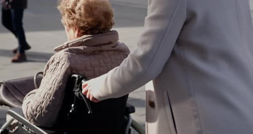 Woman Pushes Senior in Wheelchair on City Sidewalk