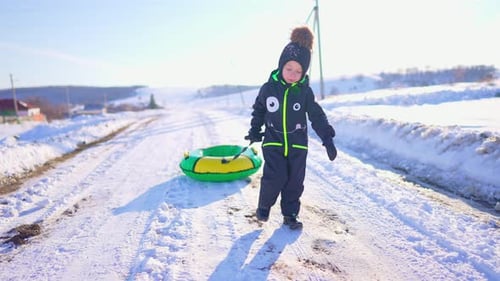 Smiling Child Pulls Snow Tube in Winter Landscape