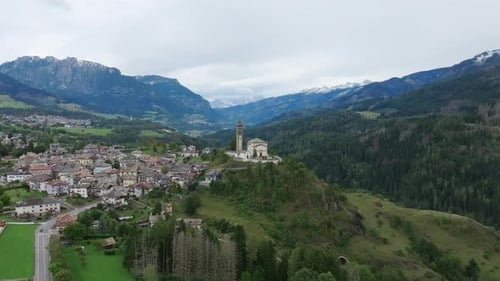 Aerial footage flying towards a church spire on a hill just outside a small Italian town.