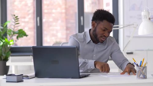 Business, People, Paperwork and Technology Concept - African American Businessman with Laptop