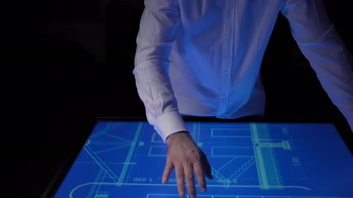 A Man in a White Shirt Moves a Blueprint with His Hand on a Large Touch Screen