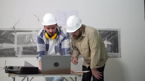 Two Construction Workers are Looking on a Laptop and Discussing the Project