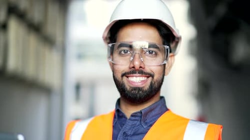 Close up portrait of young smiling professional engineer wearing safety helmet, protective glasses