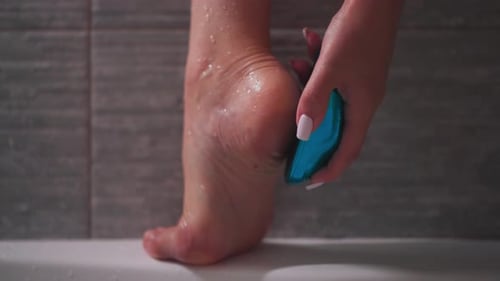 Woman Exfoliating Foot with Pumice Stone in Shower