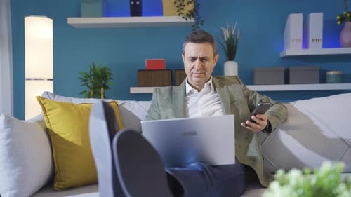 Man Using Laptop and Phone on Couch