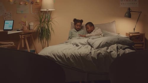 Siblings Playing on Digital Tablet in Bed at Night
