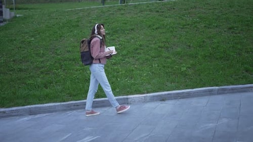 Woman with Headphones Walking and Writing in Notebook