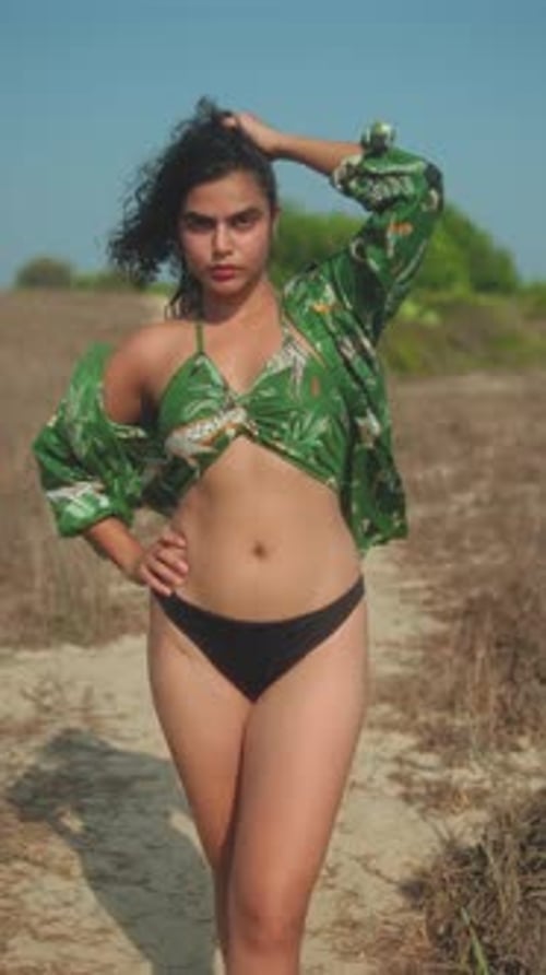 Confident young woman poses in bikini and tropical shirt on sunny dry outdoor path