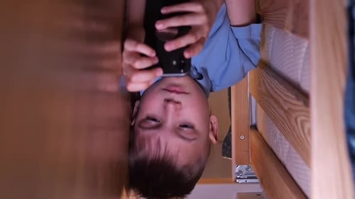 Boy Using Phone in Between Bed and Wall