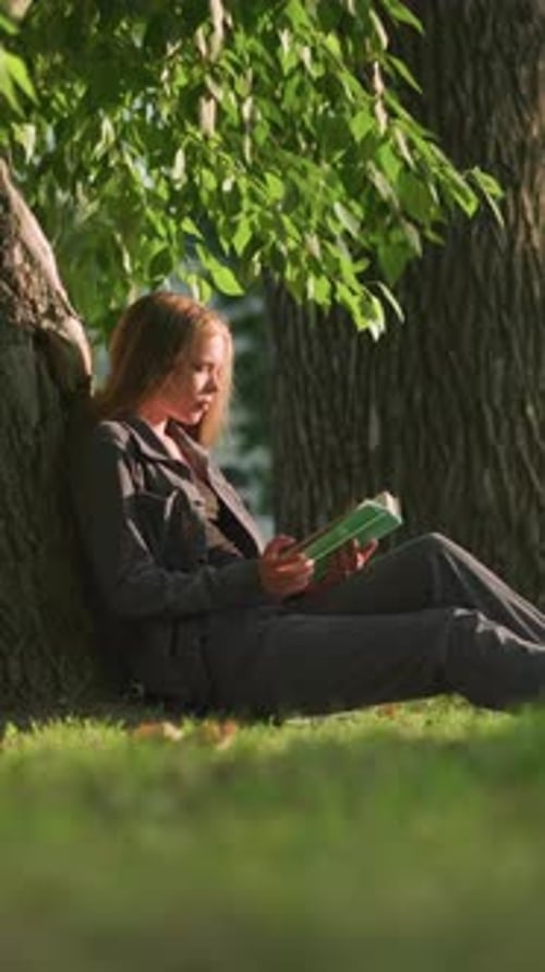 Woman Reading Book Leaning Against Tree Trunk