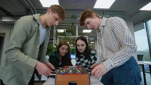Young Adults Play Foosball Table Game in Office