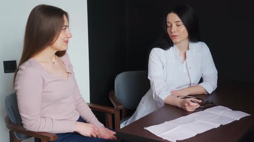 A doctor in a white coat consults a young female patient in the office of a private clinic.