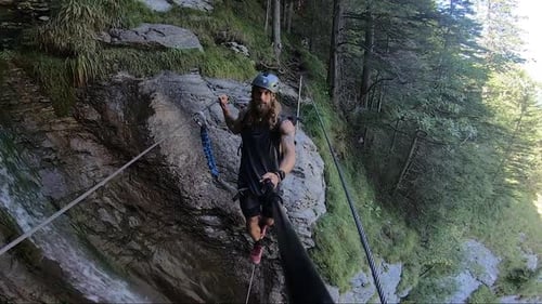 Strong young man is walking slowly and steady over a small waterfall that runs next to him in the fo