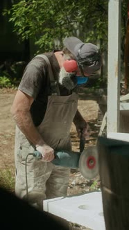 Vertical of Stone Sculptor Using Angle Grinder Outside Workshop