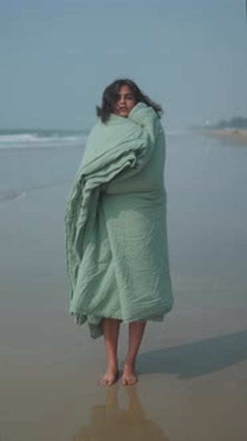 Mujer envuelta en una manta en la orilla del mar