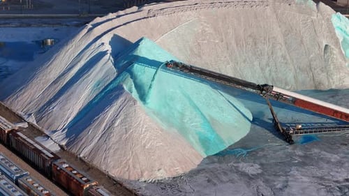 Conveyor pouring salt onto large blue-green mound at Detroit salt mine site, USA. Aerial static